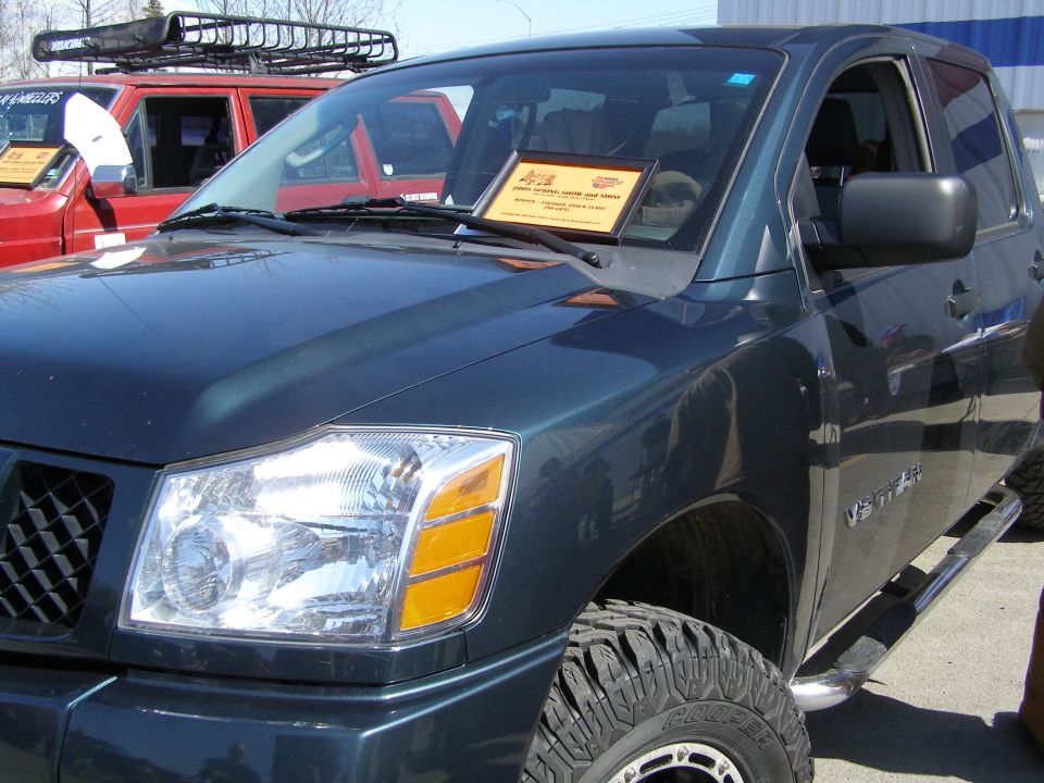 Dark green Nissan Titan pickup truck, front passenger side view, with a red Ford Bronco behind it.