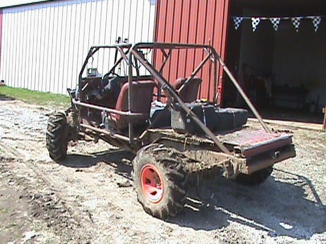 custom buggy with roll cage, large tires, and open seating, parked on dirt in front of a building