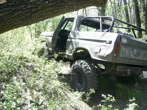 1978 Ford Bronco - A 1978 Ford Bronco navigates a wooded trail with its doors open and a roll cage visible.