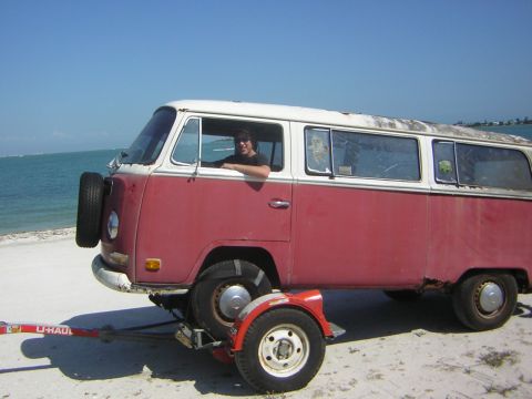 1971 Volkswagen Vanagon - A person is in the driver's seat of a red and white Volkswagen bus being towed on a trailer near the ocean.