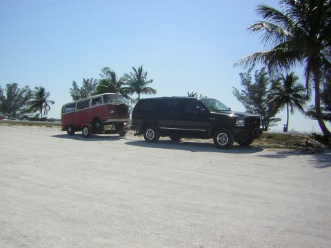 1971 Volkswagen Vanagon - A vintage Volkswagen Type 2 van is towed by a black SUV near palm trees and the ocean.