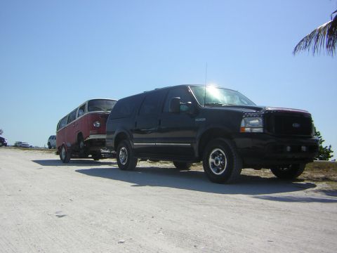 1971 Volkswagen Vanagon - A black Ford Excursion tows a red 1971 Volkswagen bus on a dirt road under a clear blue sky.