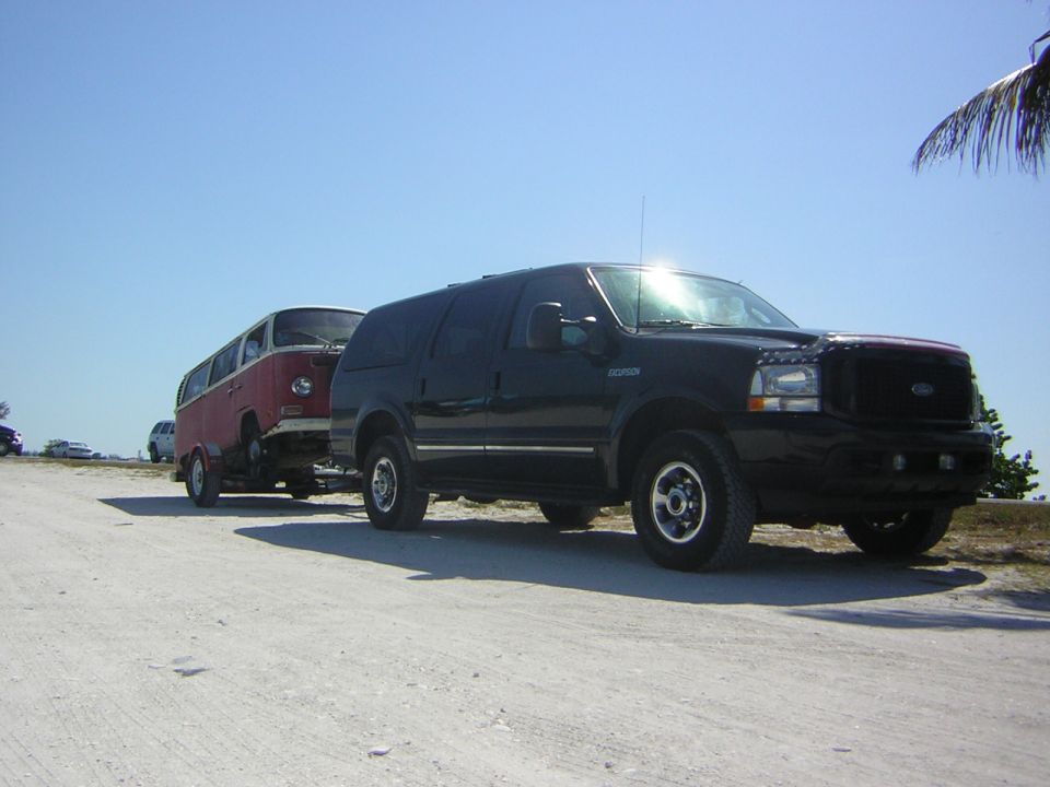 1971 Volkswagen bus being towed by a black Ford Excursion on a dirt road