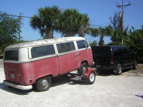 1971 Volkswagen Vanagon - A vintage red and white Volkswagen bus is towed by a black SUV under a clear blue sky with palm trees.