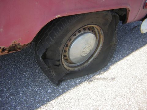 1971 Volkswagen Vanagon - Flat tire on a red vehicle, showing rust damage on the fender and a deflated tire.