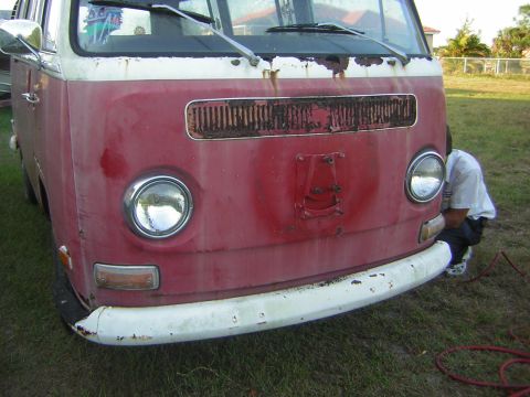 1971 Volkswagen Vanagon - A red and white Volkswagen Type 2 van, likely from the late 1960s, shows signs of wear and tear, with a person attending to the front.