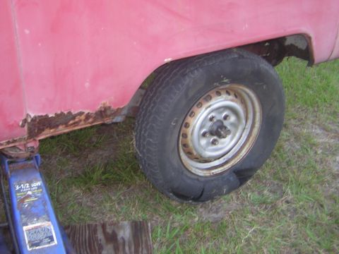 1971 Volkswagen Vanagon - A flat tire and significant rust are visible on the rear wheel well of a red van.