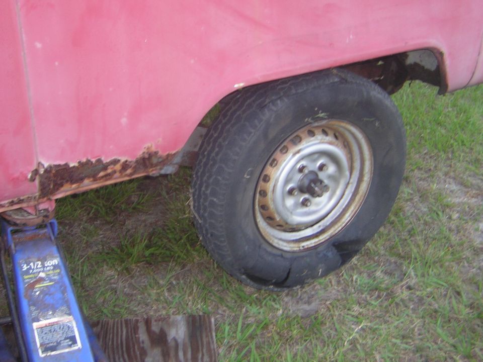 Red van rear wheel well with rust and flat tire on a jack