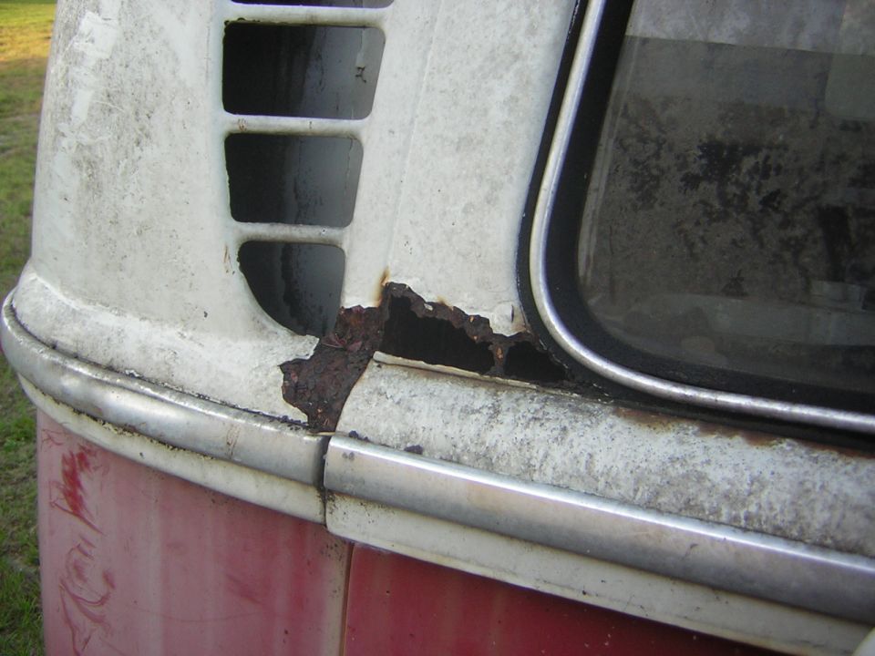 Close-up of rust on the rear corner of a white and red VW van.