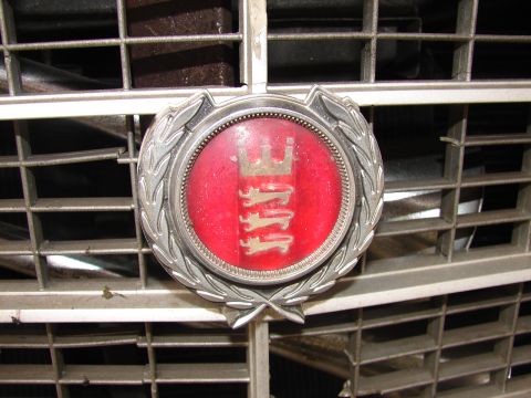 1973 Ford Ranchero - Close-up of a round chrome-and-red enamel grille badge showing a crown above three stacked lions, framed by a laurel-wreath surround. The m…