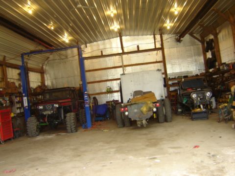 1992 Ford Bronco - A garage scene three off-road vehicles, one of which is elevated on a car lift.