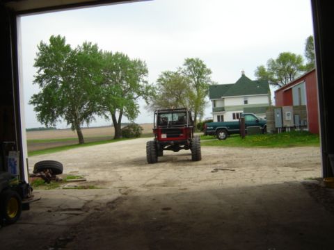 1992 Ford Bronco - A red off-road vehicle is parked outside a garage, with a green pickup truck and a house in the background.