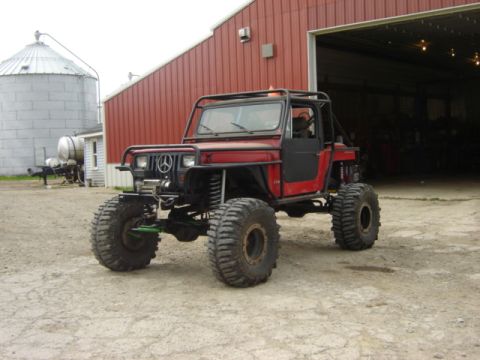 1992 Ford Bronco - A heavily modified off-road vehicle with a custom roll cage and large tires sits in front of a red barn.