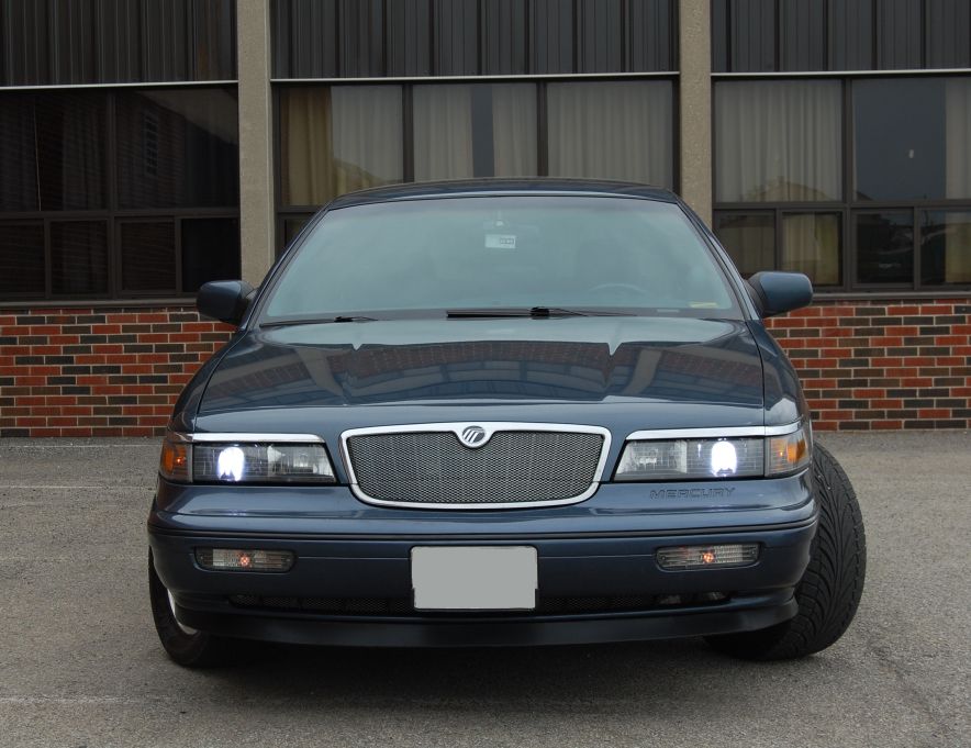 Front view of dark blue Mercury Grand Marquis with chrome grille and lit headlights