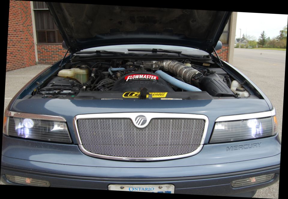 Slate-blue Mercury Grand Marquis with hood up showing cold-air intake and mesh grille