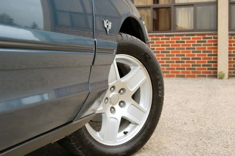 1985 Mercury Grand Marquis - Close-up of a blue sedan's side, showing a chrome wheel and a fender emblem.