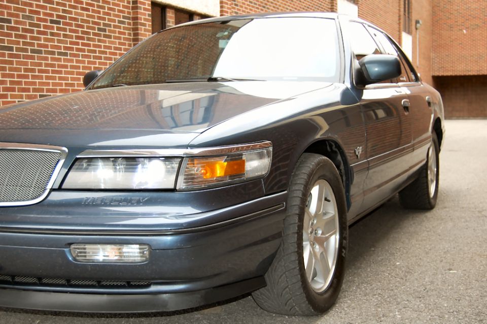 Dark blue Mercury Grand Marquis front corner against a brick wall
