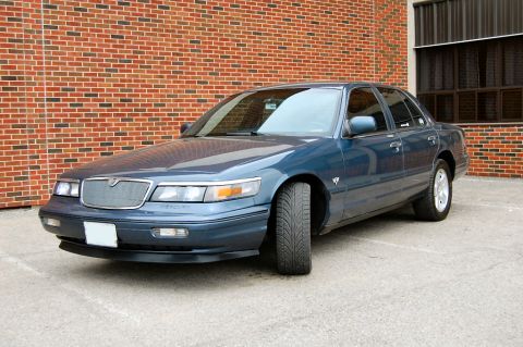 1985 Mercury Grand Marquis - A blue Mercury Grand Marquis is parked outside a building with a brick facade.