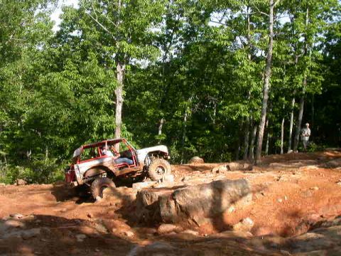 1990 Ford Bronco - An off-road vehicle tackles a challenging rocky course surrounded by lush green trees.