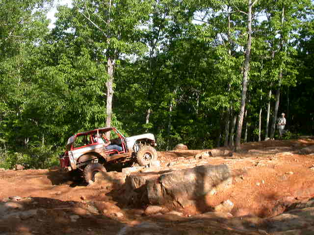 White off-road vehicle with red roll cage navigating rocky terrain