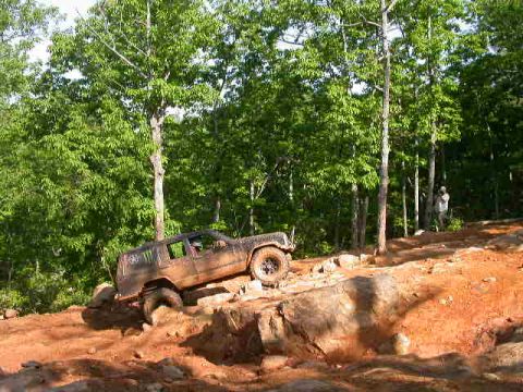 1990 Ford Bronco - An off-road vehicle navigates a challenging rocky terrain surrounded by trees.