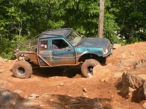 1990 Ford Bronco - A teal off-road truck navigates a challenging rocky course.