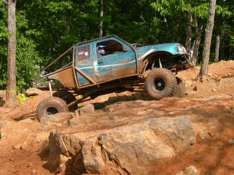 1990 Ford Bronco - A heavily modified blue truck with a roll cage tackles a challenging rocky obstacle course.