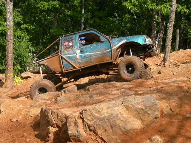 Blue off-road truck with roll cage navigating rocky terrain