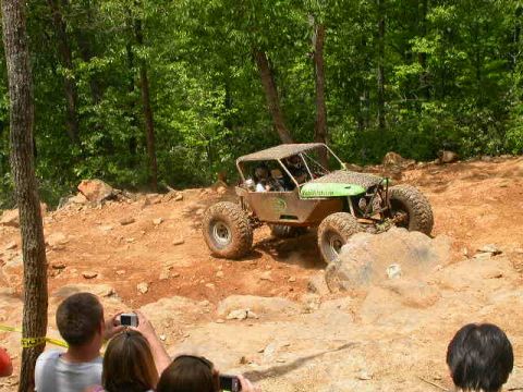 1990 Ford Bronco - An off-road buggy navigates a challenging rocky terrain, kicking up a cloud of dust.