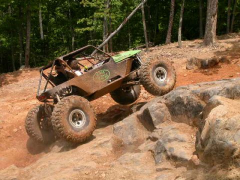 1990 Ford Bronco - This heavily modified buggy is navigating a rocky obstacle on a wooded trail.