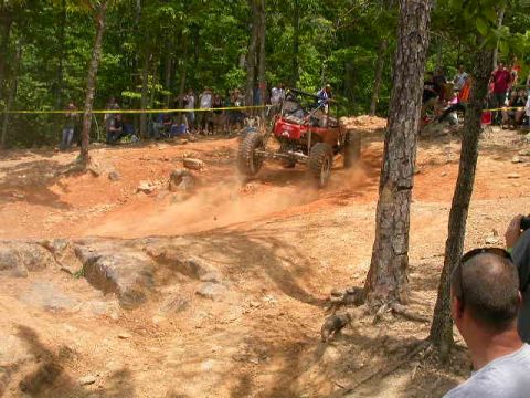1990 Ford Bronco - An off-road buggy navigates a dusty track during a race event, with onlookers gathered to watch.
