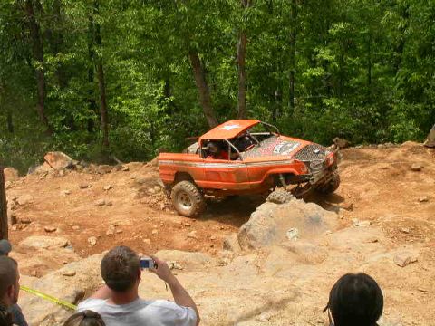 1990 Ford Bronco - An orange off-road vehicle tackles a rocky course during an event.