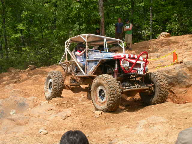 Off-road buggy with a roll cage climbing a dirt hill. Red bars protect the front