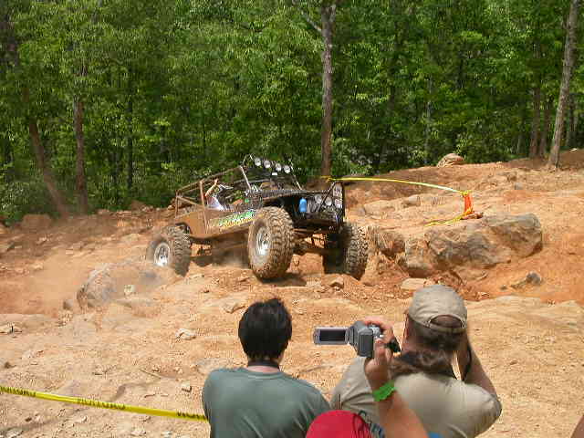 Off-road buggy climbing a rocky hill, with spectators filming