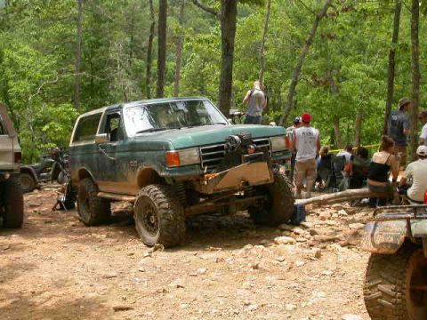 1990 Ford Bronco - A modified green Ford Bronco navigates a rocky off-road trail with spectators present.