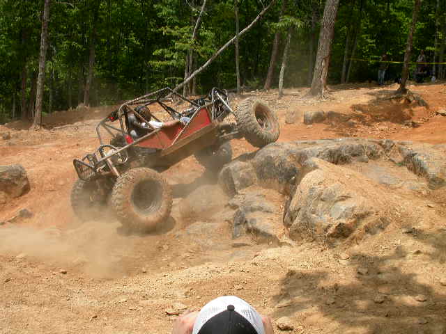 Red off-road buggy climbing a rocky incline, kicking up dust