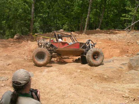 1990 Ford Bronco - A custom off-road buggy navigates a rocky, wooded terrain.