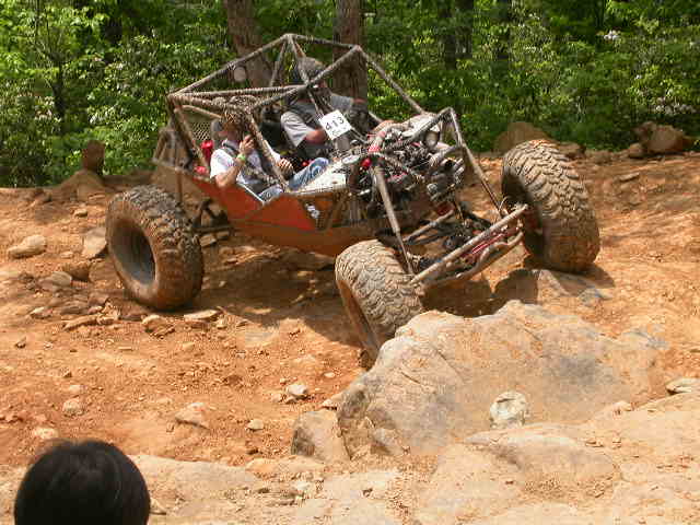 Off-road buggy with a roll cage climbing over rocks. Two people are inside