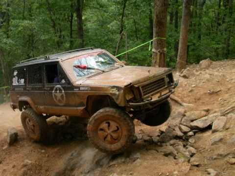 1990 Ford Bronco - A muddy Jeep Cherokee XJ navigates a challenging off-road course.