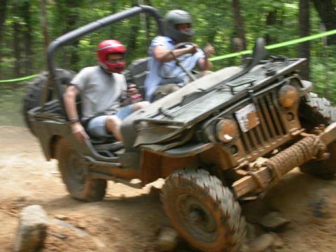 1990 Ford Bronco - Two individuals in helmets navigate a off-road course in a vintage-style jeep.