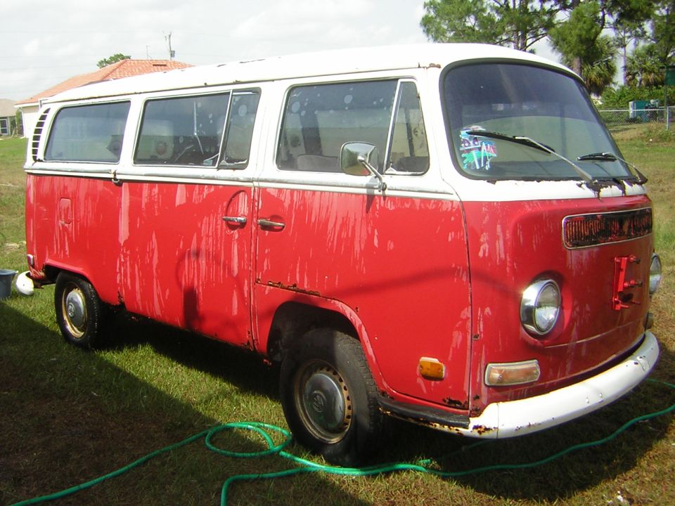 Red and white Volkswagen bus parked on grass with a green hose