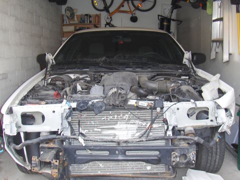 2003 Ford Crown Victoria - Front view of a damaged 2003 Ford Crown Victoria with its hood open, revealing the engine compartment.