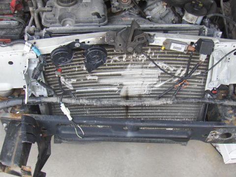 2003 Ford Crown Victoria - The front end of a white vehicle shows a damaged radiator and exposed engine parts, indicating significant impact.