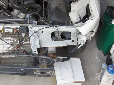 2003 Ford Crown Victoria - The front end of a white vehicle shows significant damage, with exposed radiator and engine parts visible.