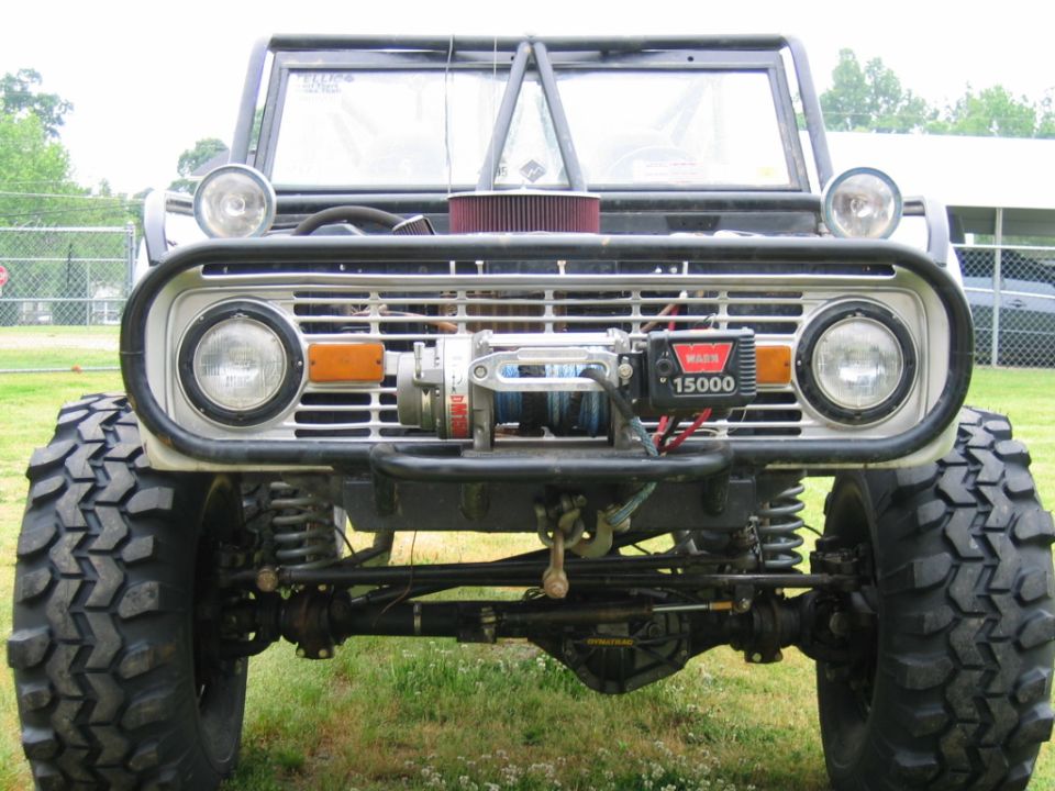 Front view of a modified 1974 Ford Bronco with large off-road tires, a winch, and a roll cage