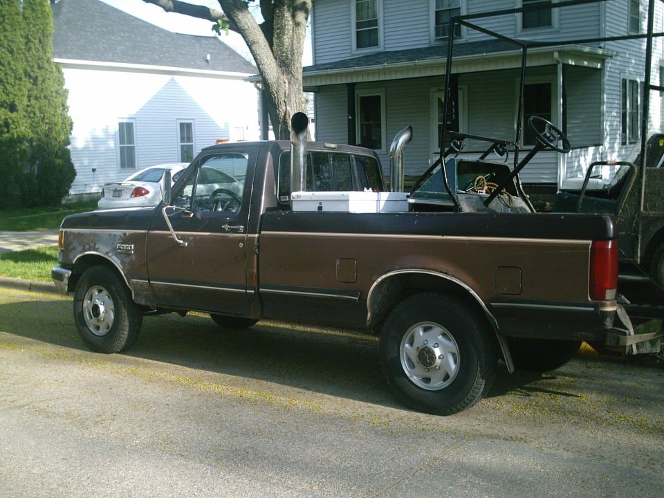 Brown two-tone Ford regular-cab pickup with twin chrome exhaust stacks and loaded bed parked on a street