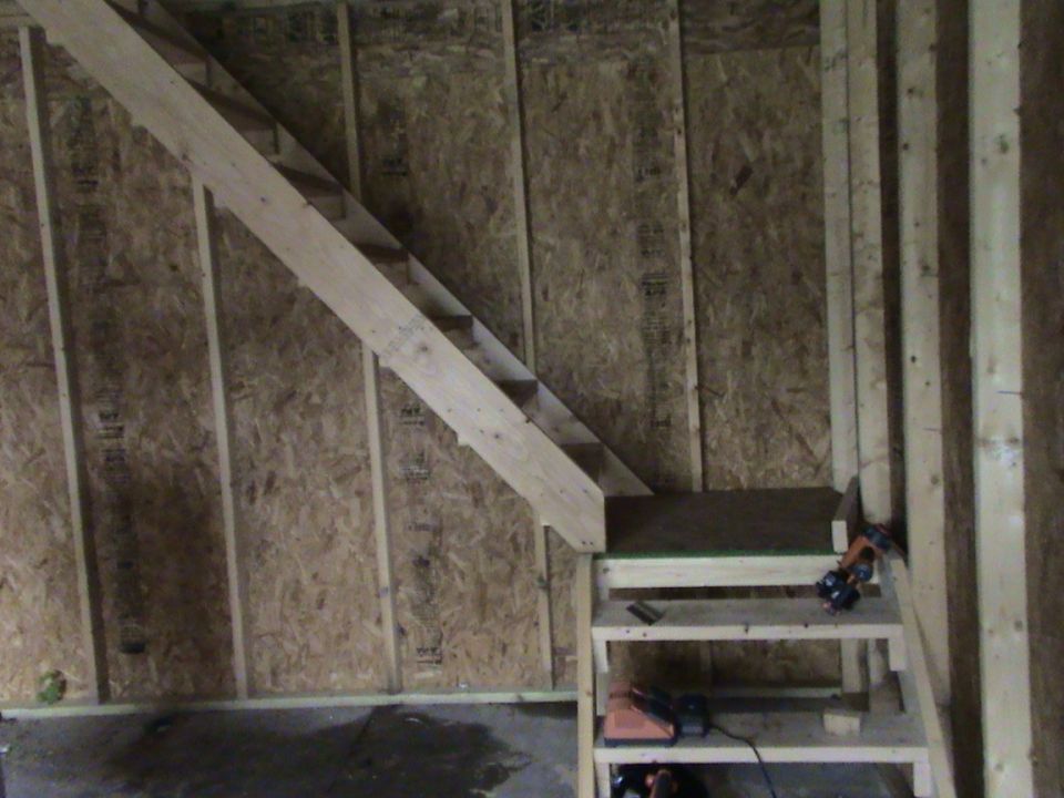 Unfinished wooden staircase and shelving unit in a room with OSB walls