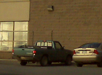 1996 Ford Bronco - A pickup truck and a car are parked outside a building.