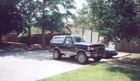 1990 Ford Bronco - A black Ford Bronco is parked in a residential driveway under leafy trees.