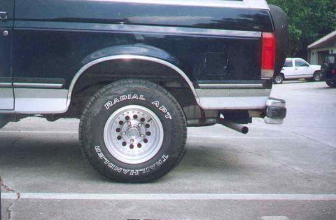 1990 Ford Bronco - Rear quarter panel and wheel of a 1990 Ford Bronco, with a white SUV visible in the background.
